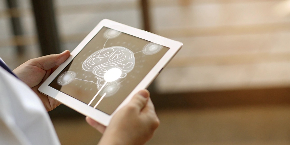 Person holding a tablet that shows a stylized brain schematic on the screen.