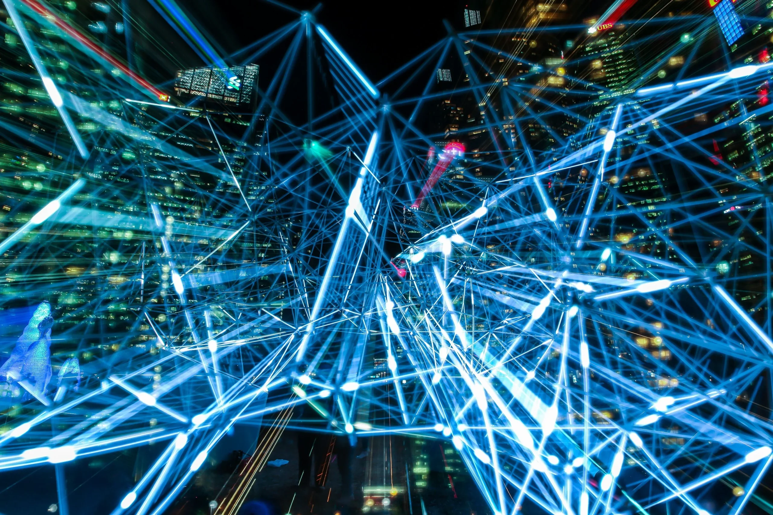 Night city skyline illuminated by crisscrossing blue laser beams in a night light show.