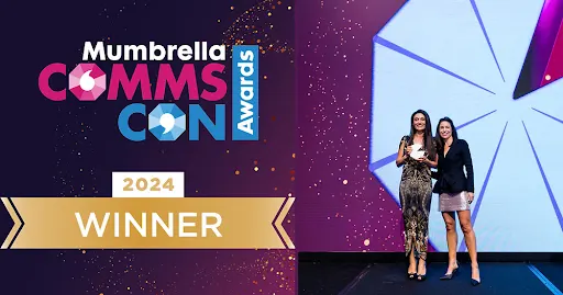 Two women on stage accepting a trophy at the Mumbrella CommsCon Awards 2024, with a WINNER banner visible.